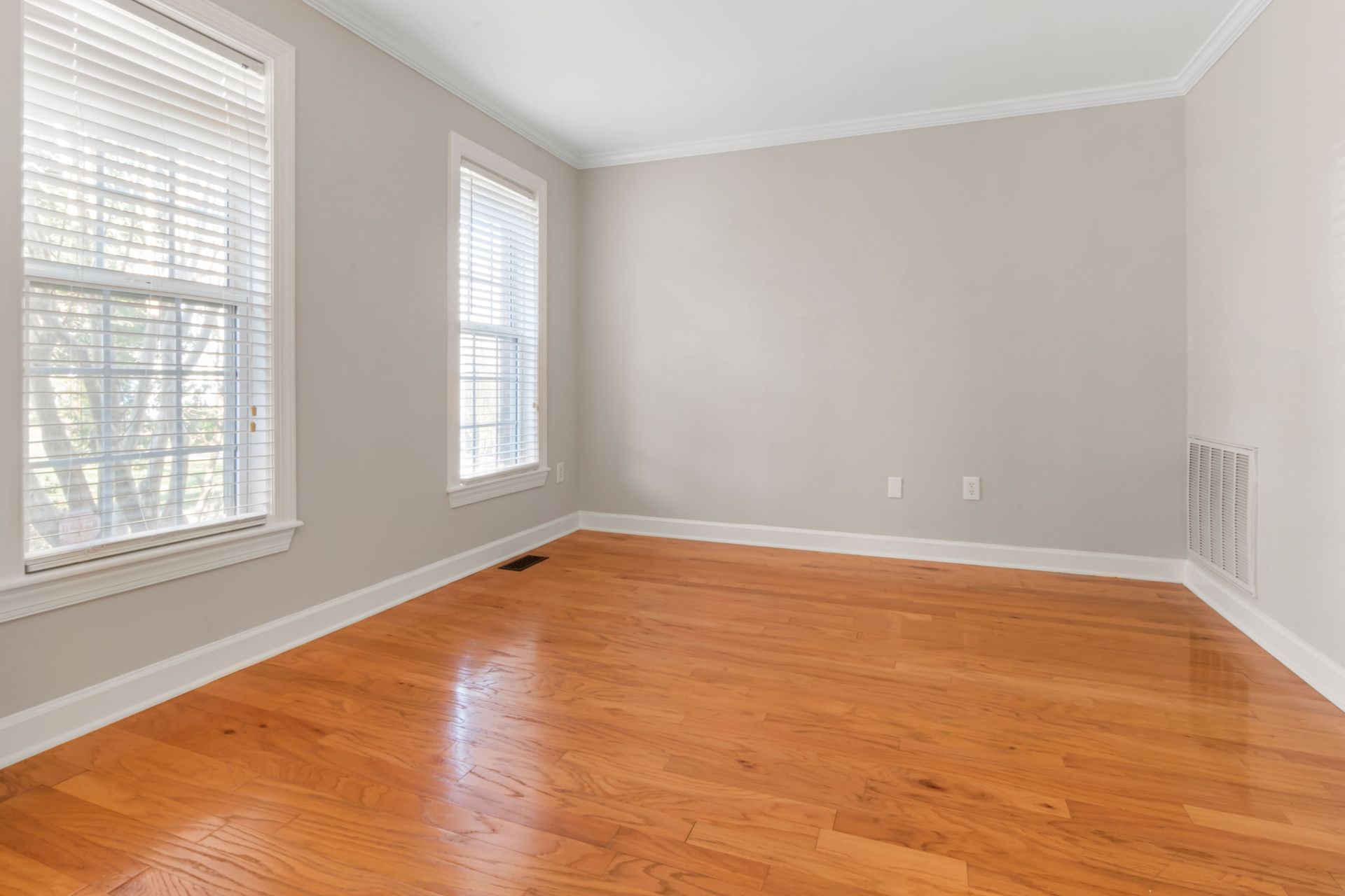 Spacious empty room with natural light, hardwood floors, and neutral walls.